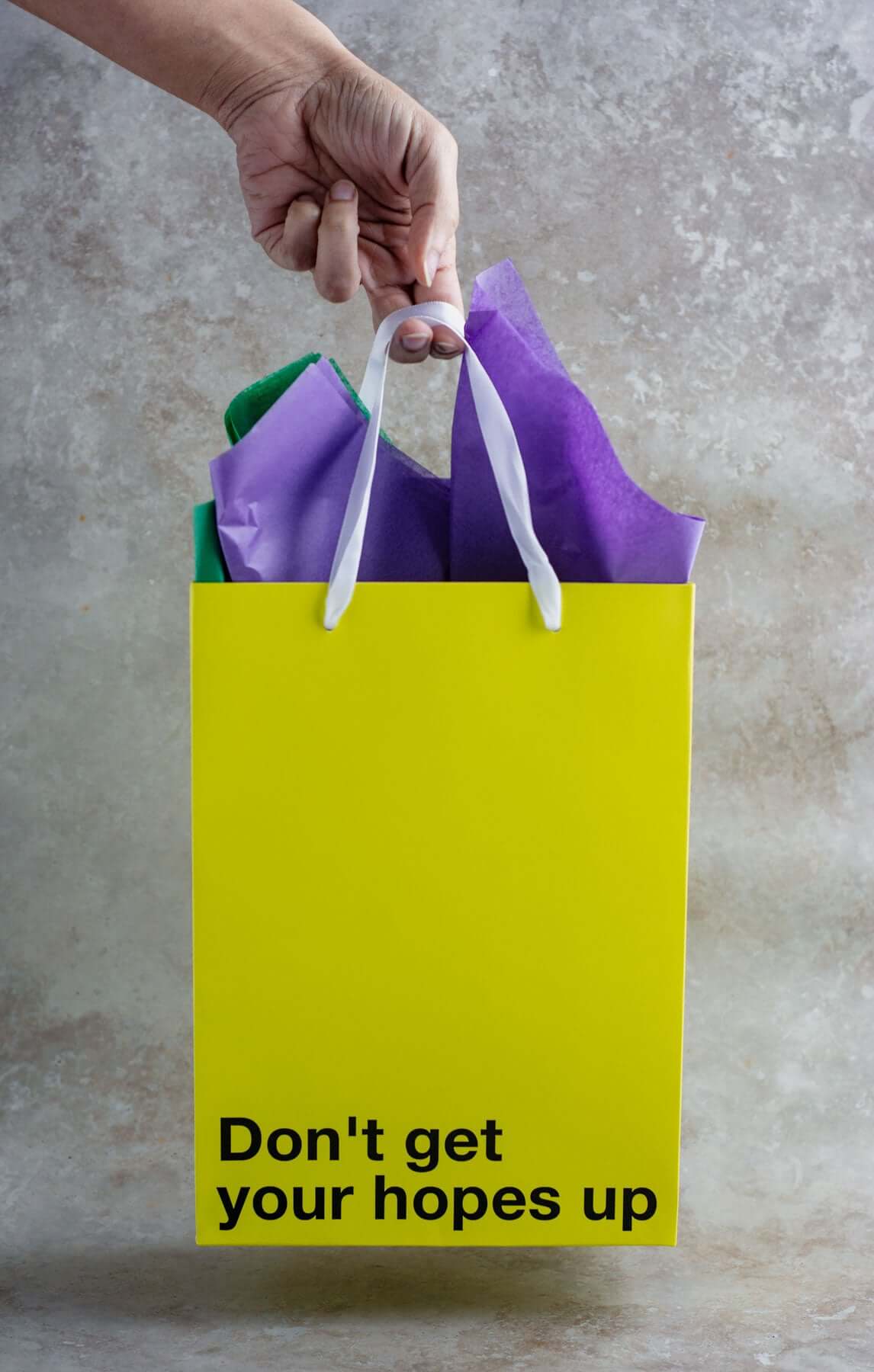 Hand holding a yellow gift bag that says "Don't get your hopes up". Ideal for funny gift bag use.