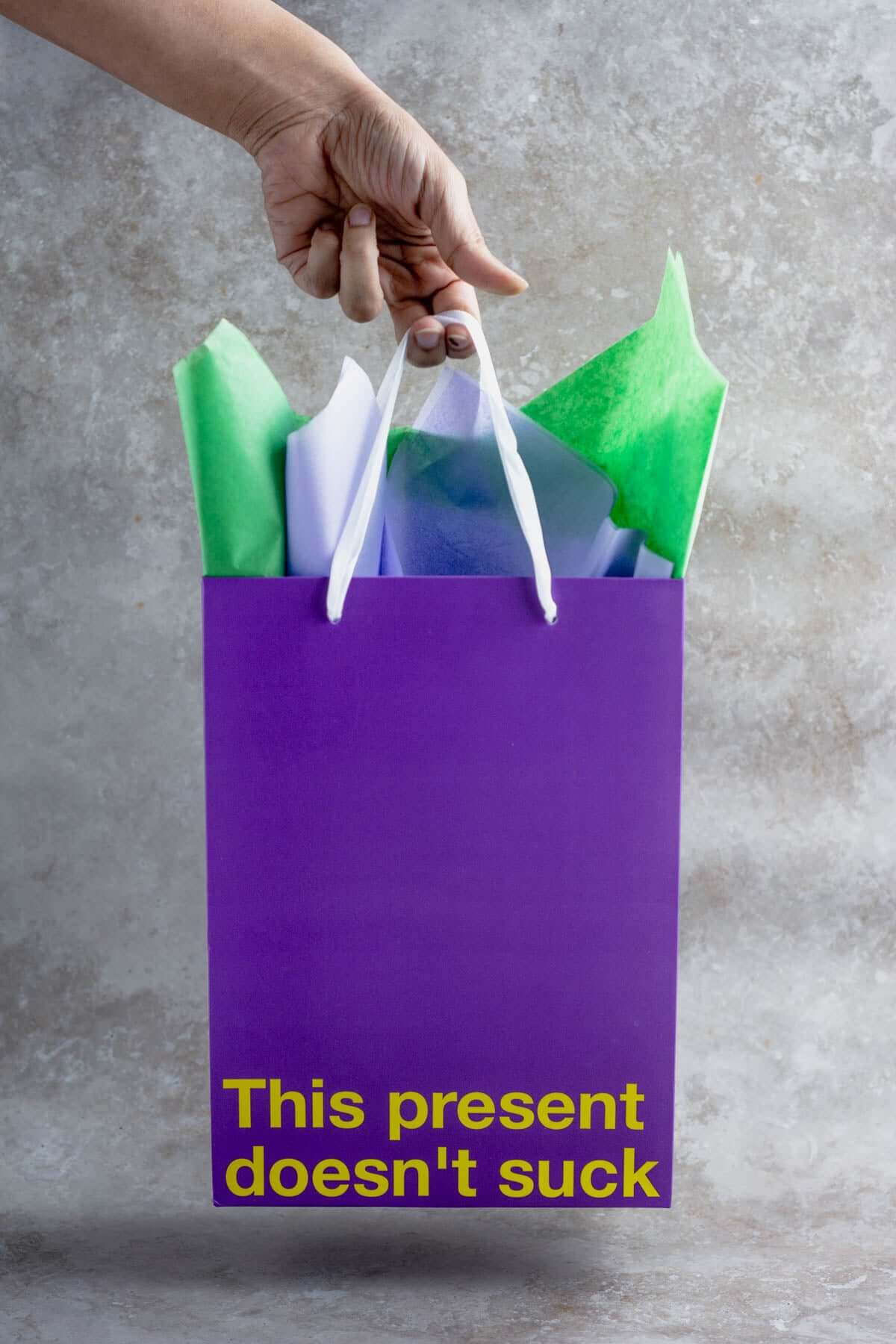 Funny gift bag, purple gift bag with green and white tissue paper, text reads 'This present doesn't suck'.