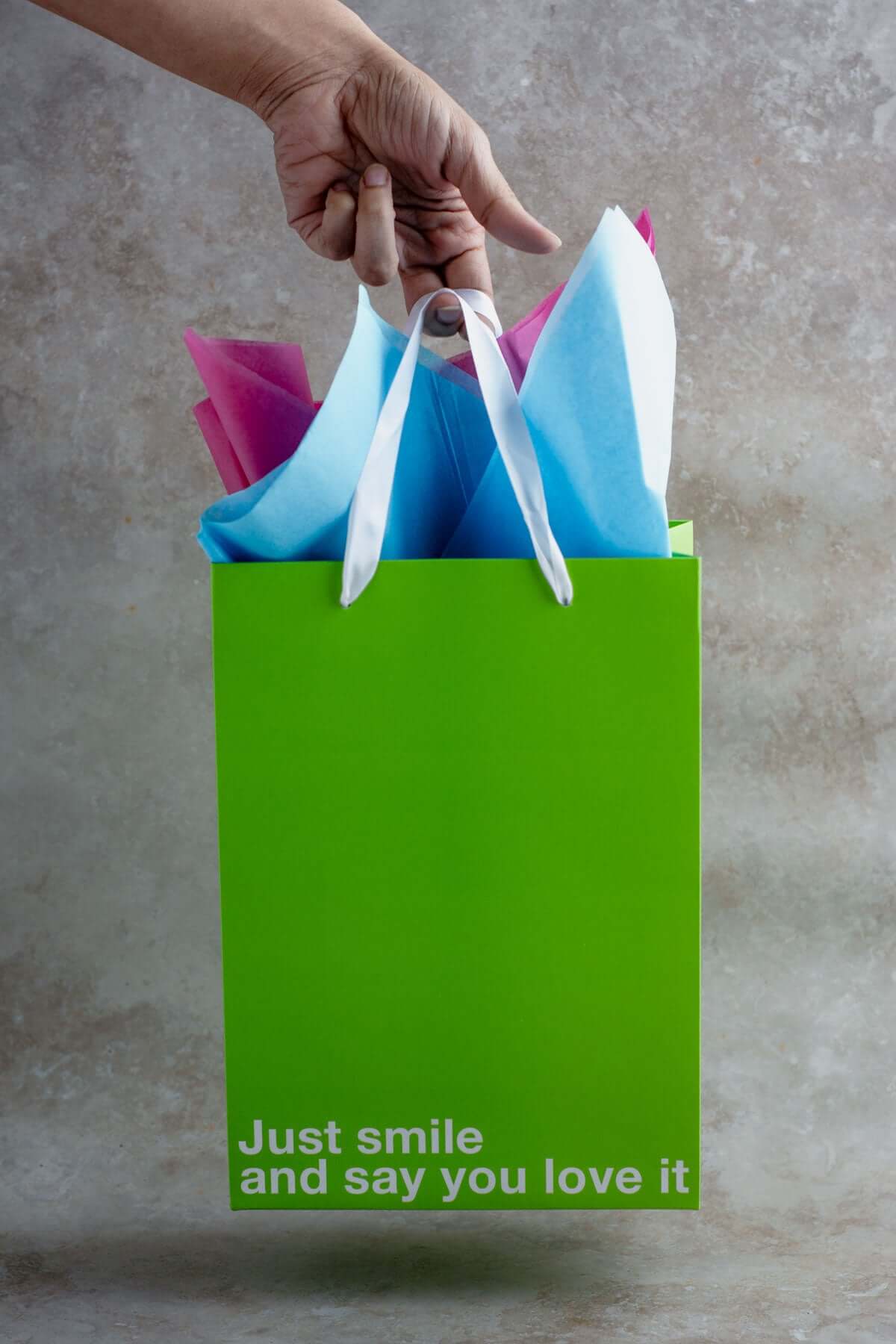 Funny gift bag in bright green with the phrase 'Just smile and say you love it', filled with colorful tissue paper.