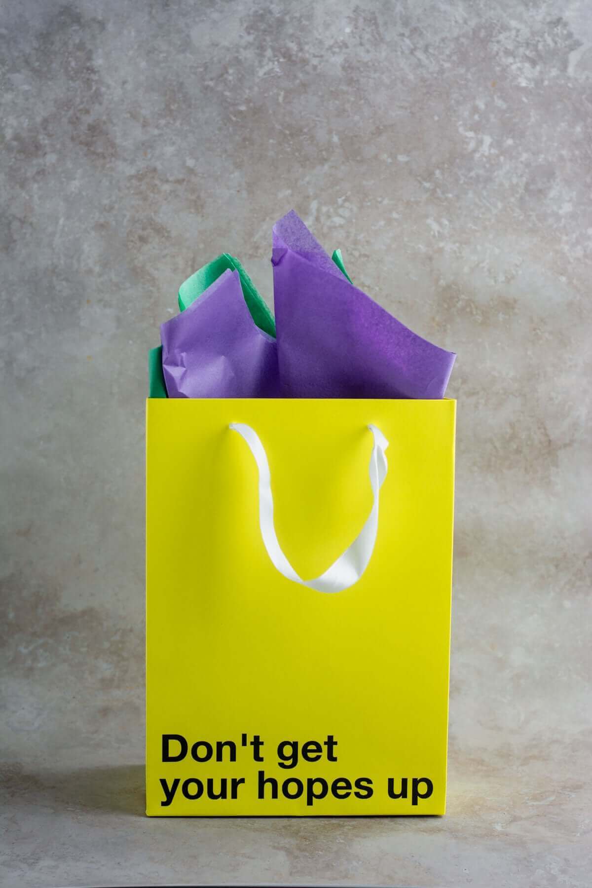 Yellow gift bag with the text 'Don't get your hopes up' and colorful tissue paper, ideal for funny gift bags.