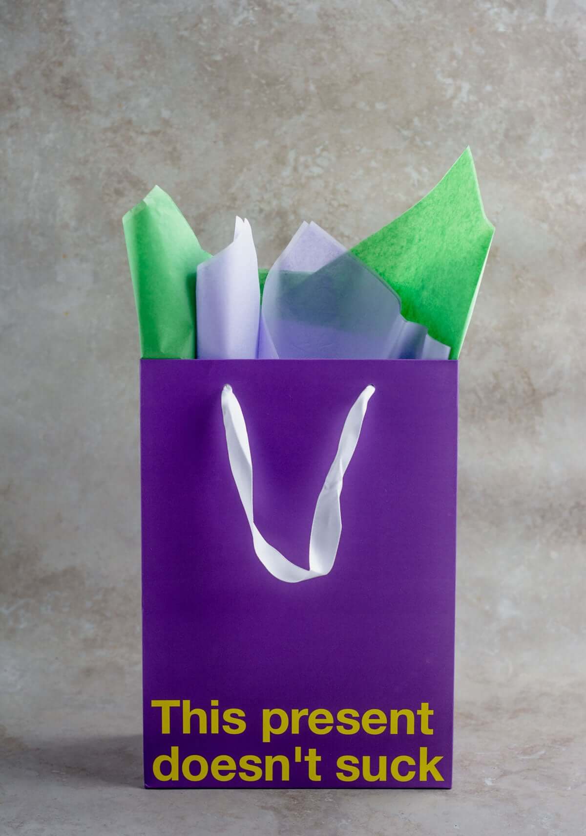 Funny gift bag in purple with the message 'This present doesn't suck' and colorful tissue paper.