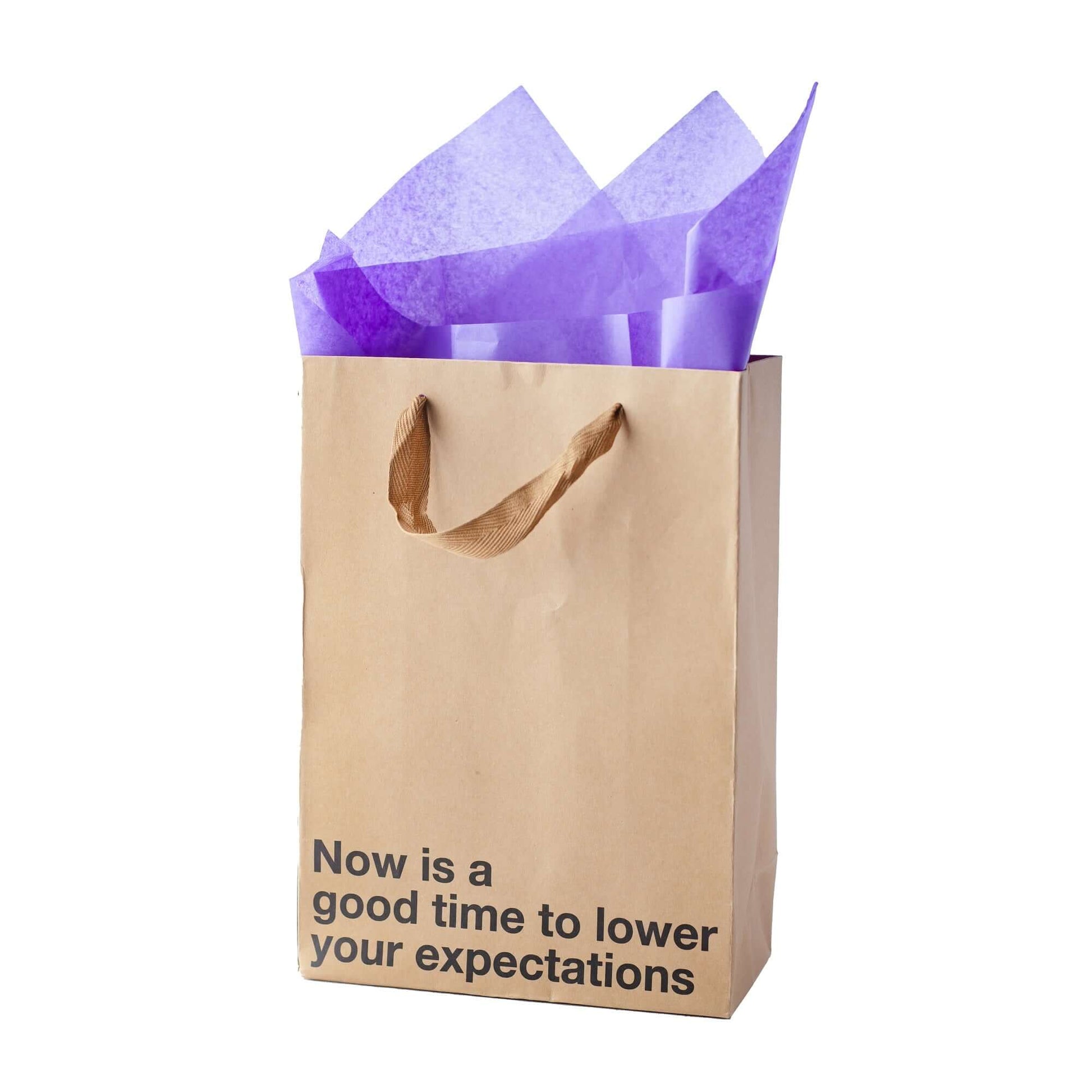 Funny gift bag with purple tissue paper and a message reading 'Now is a good time to lower your expectations'.