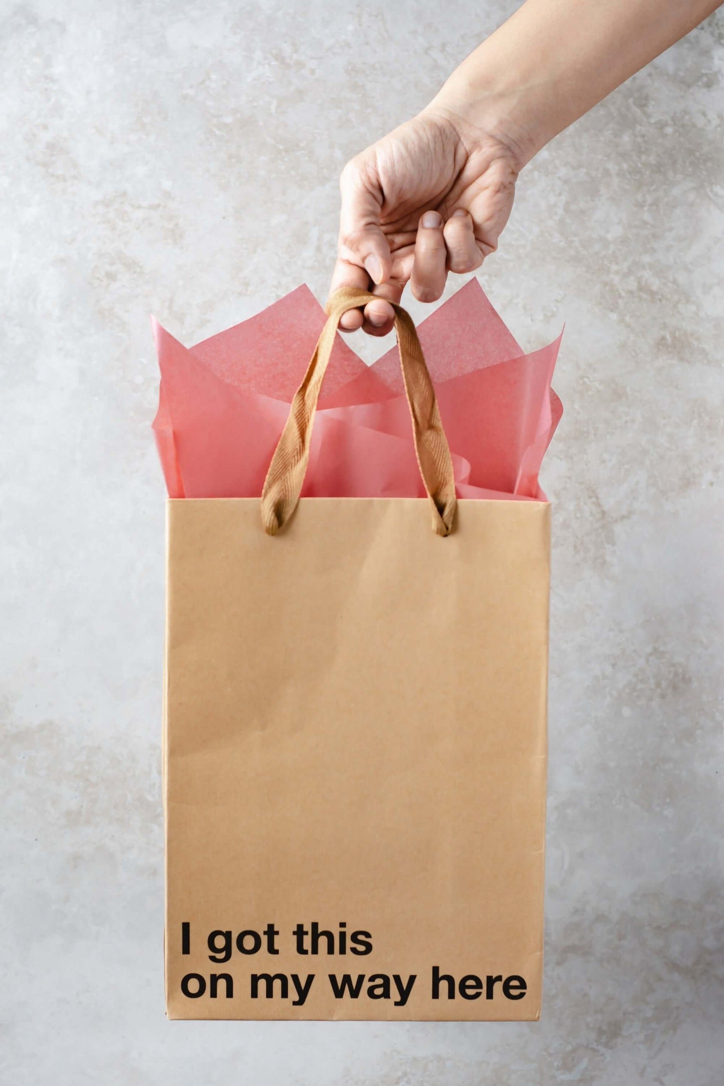 Funny gift bag with the phrase 'I got this on my way here,' held with brown ribbon handle against a neutral background.