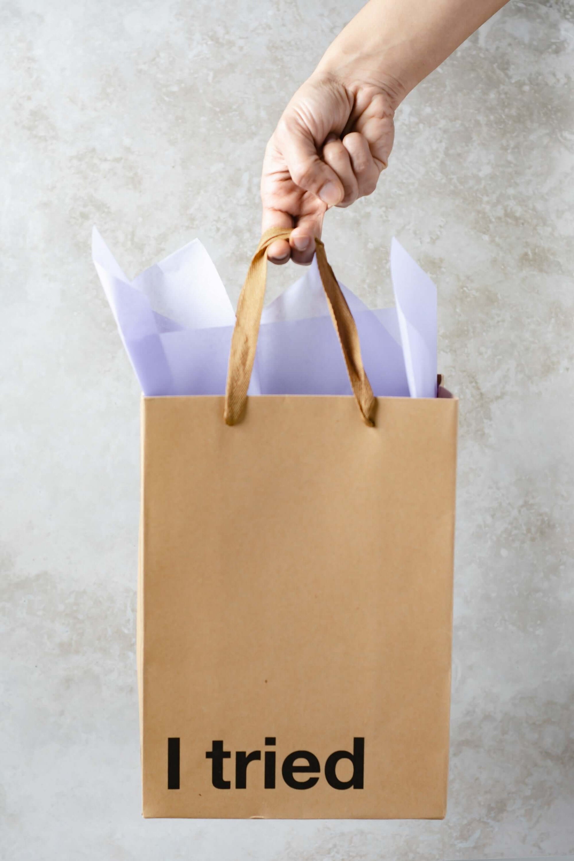 Hand holding a kraft gift bag with the text 'I tried', showcasing a funny gift bag for unique gifting.