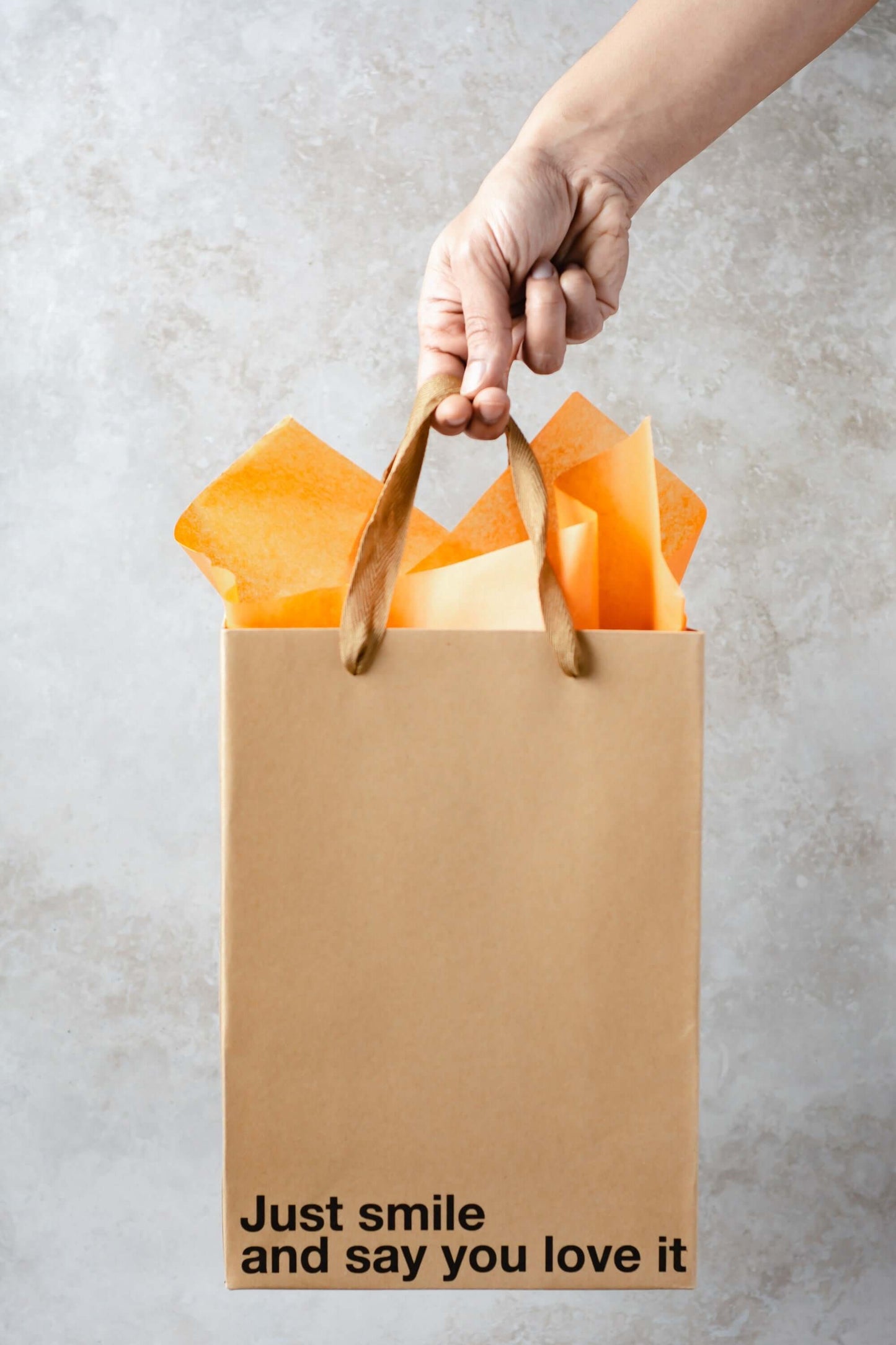 Just Smile gift bag with orange tissue paper, a funny gift bag for unique occasions, held by a hand.
