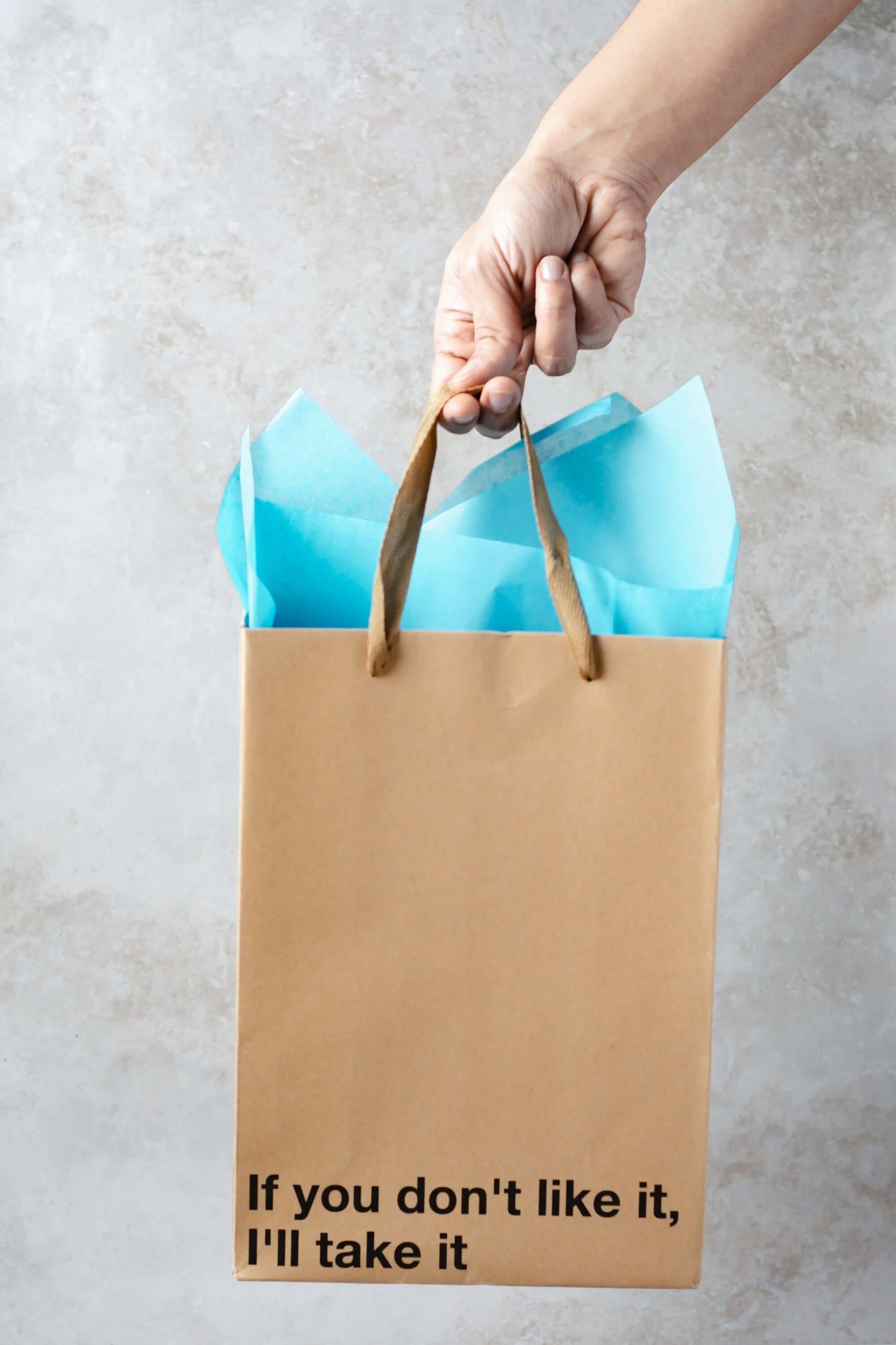 Funny gift bag with a humorous message, featuring light blue tissue paper and brown ribbon handles, suitable for any occasion.