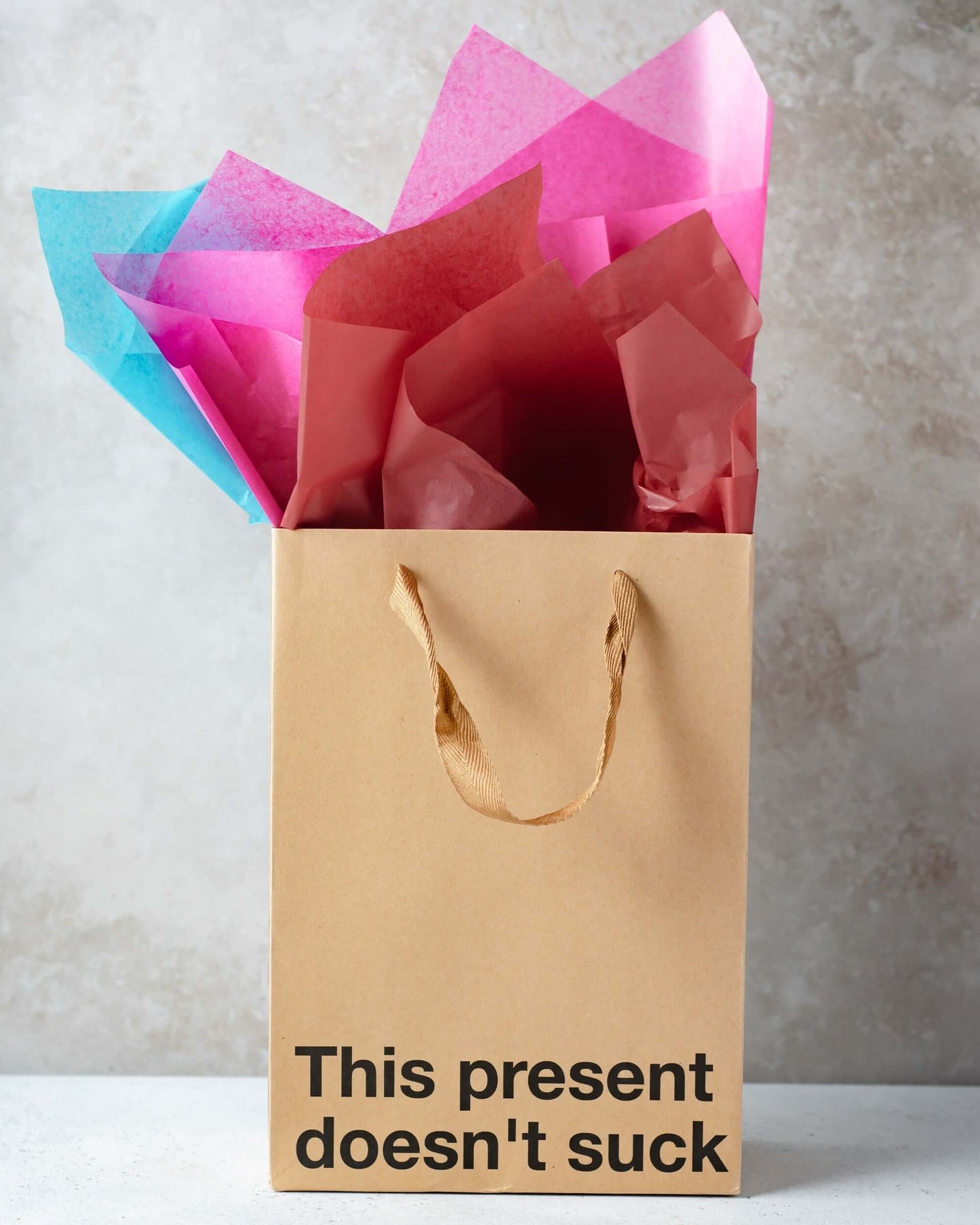 Funny gift bag with the phrase 'This present doesn't suck' and colorful tissue paper.