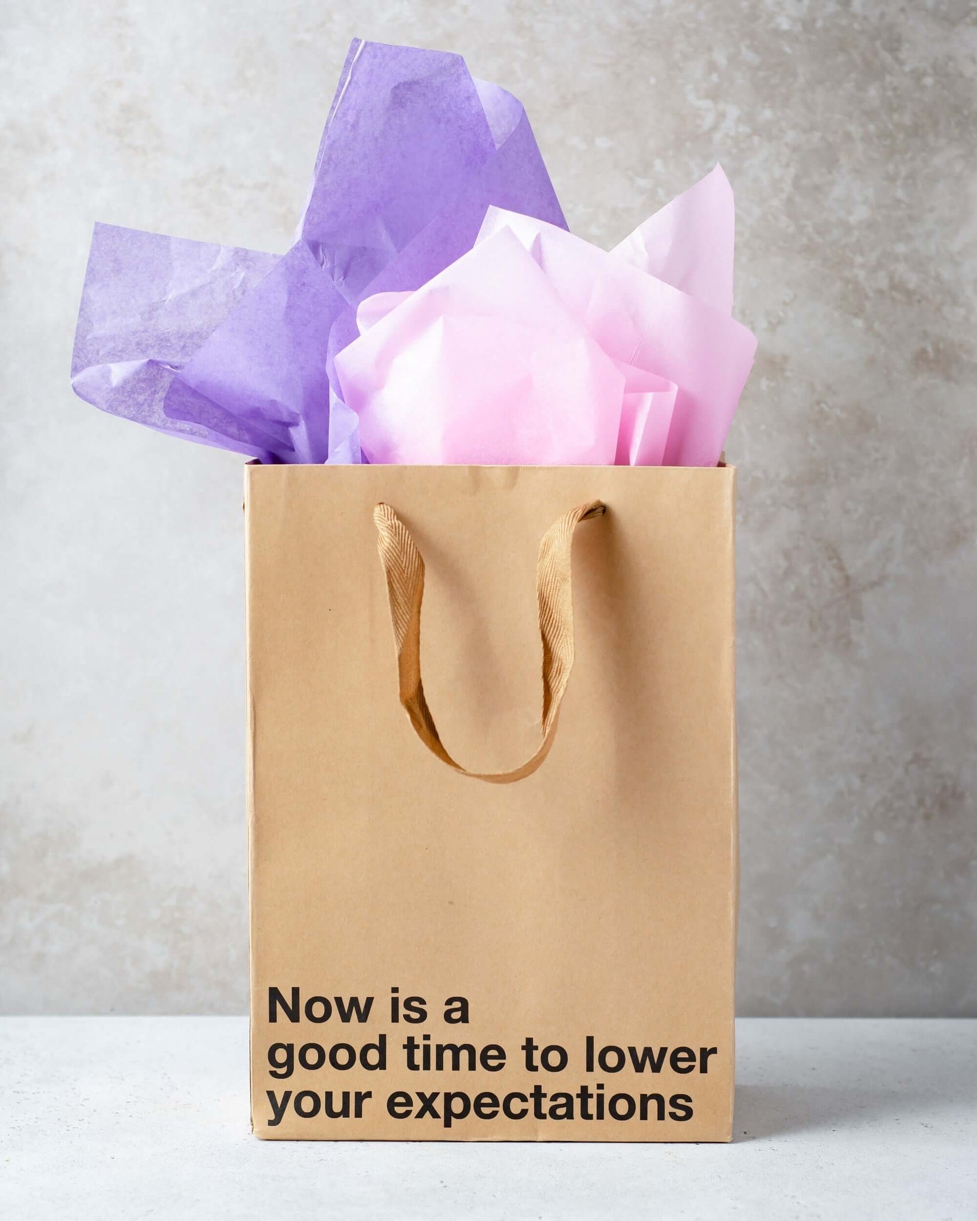 Funny gift bag with purple and pink tissue paper, featuring the phrase 'Now is a good time to lower your expectations'.