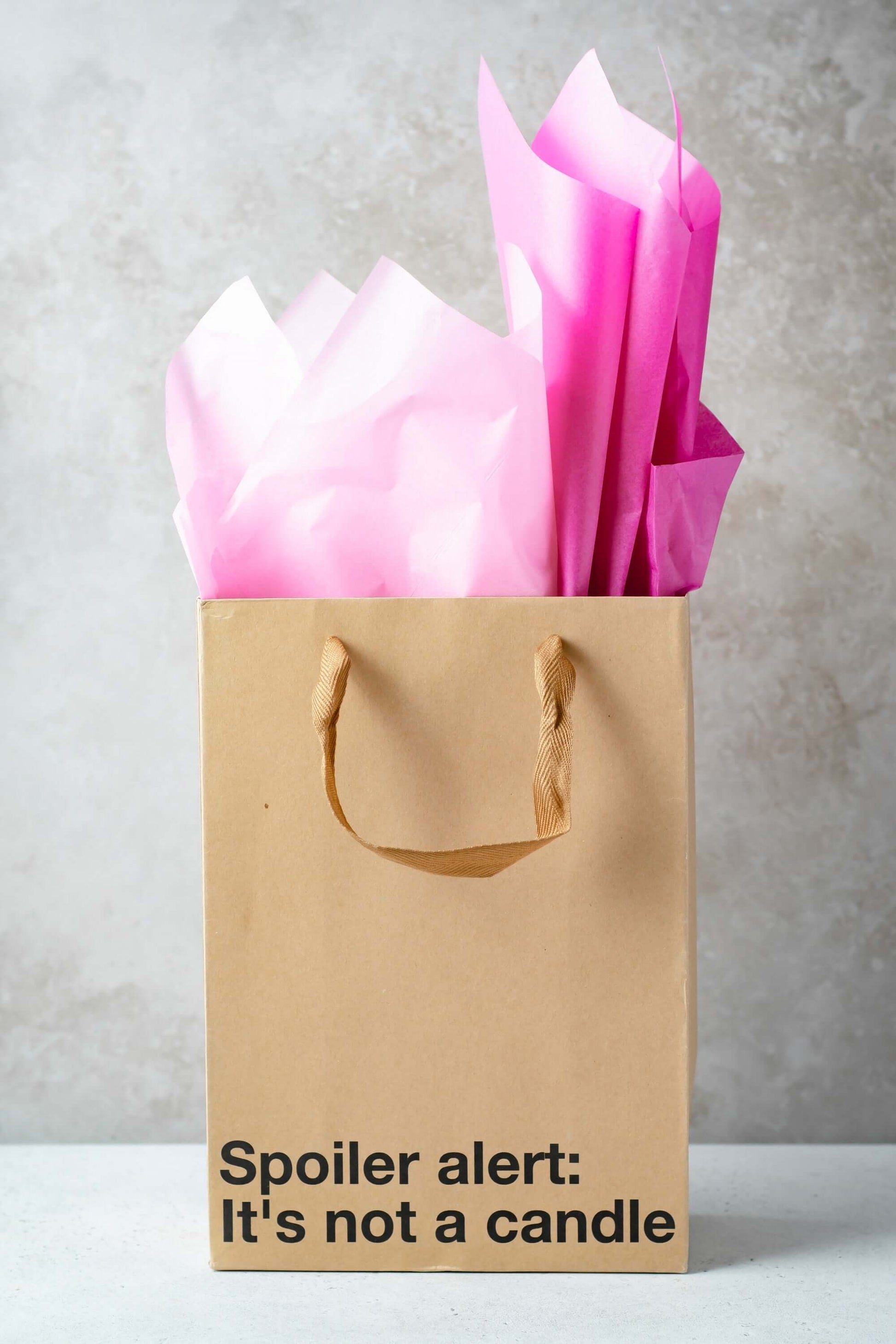 Funny gift bag featuring pink tissue paper and a humorous message: 'Spoiler alert: It's not a candle'.
