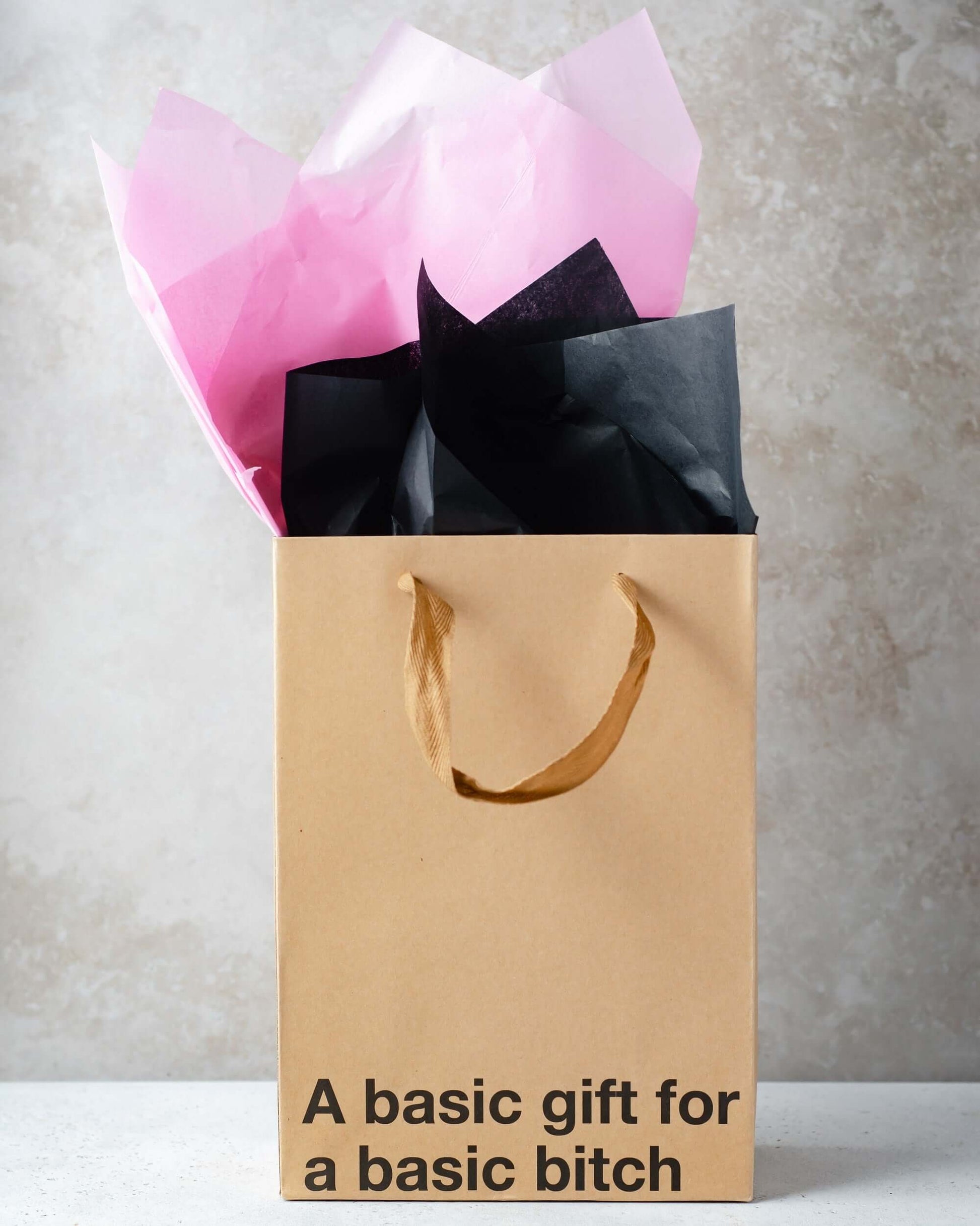 Funny gift bag with brown ribbon handle and colorful tissue paper, featuring the text 'A basic gift for a basic bitch'.