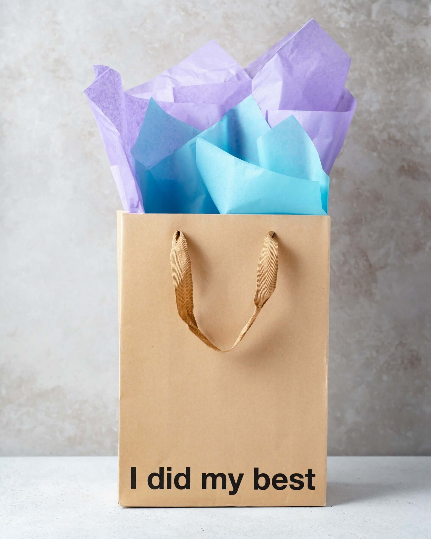 Funny gift bag with kraft material and brown ribbon handle, filled with blue and purple tissue paper.