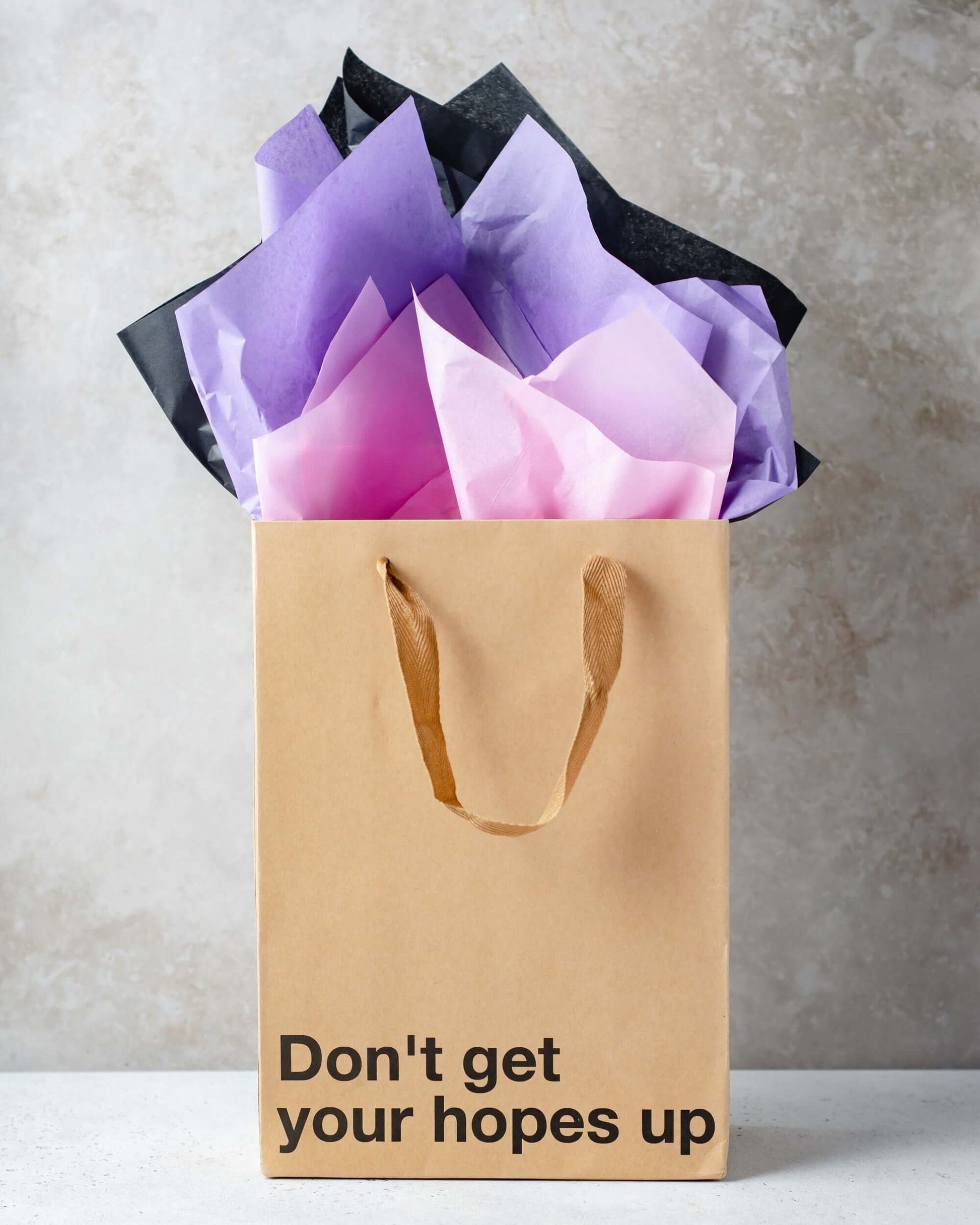 Funny gift bag with the phrase 'Don't get your hopes up' and colorful tissue paper on top.