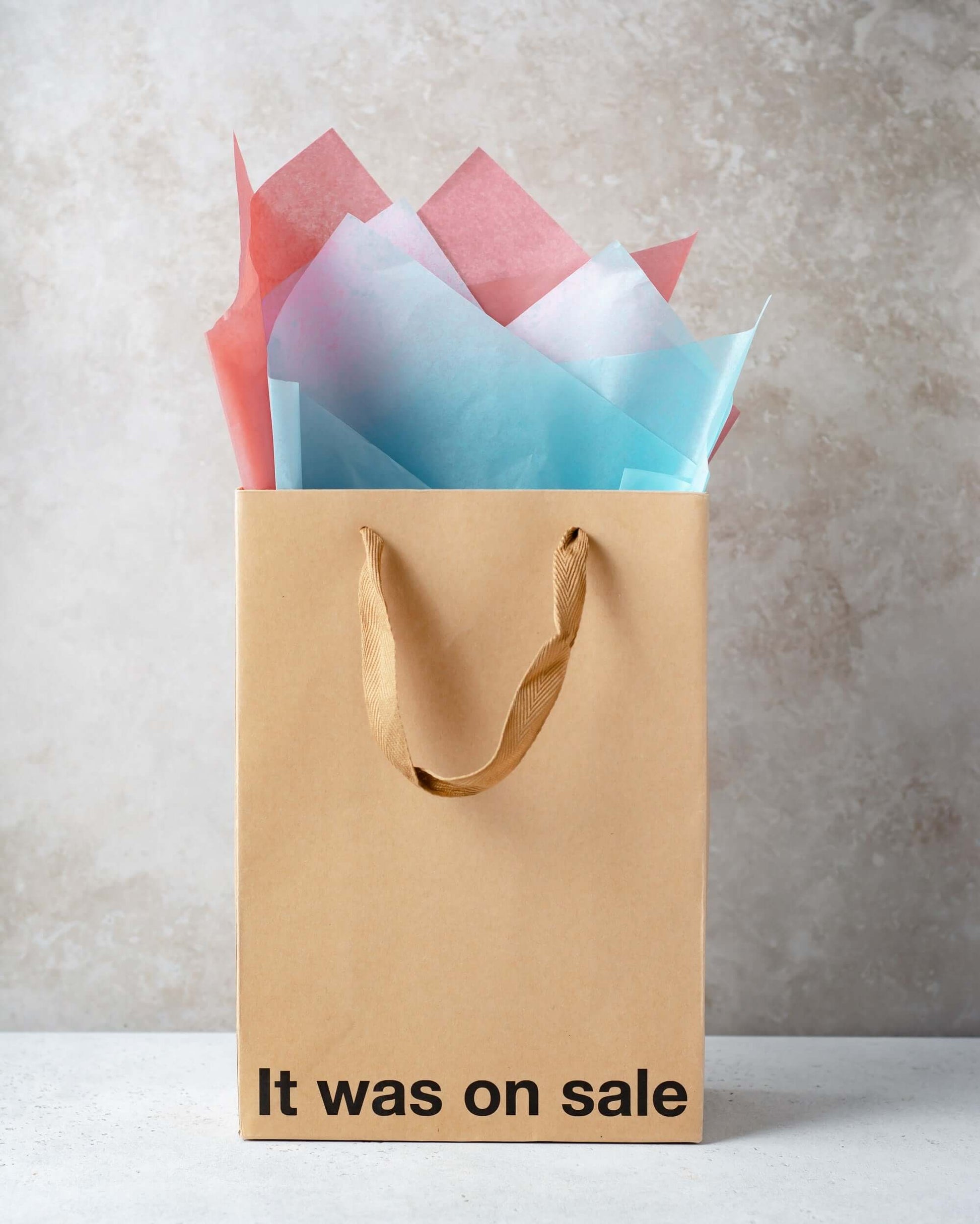 Funny gift bag with colorful tissue paper peeking out, featuring the text 'It was on sale' on a kraft paper design.