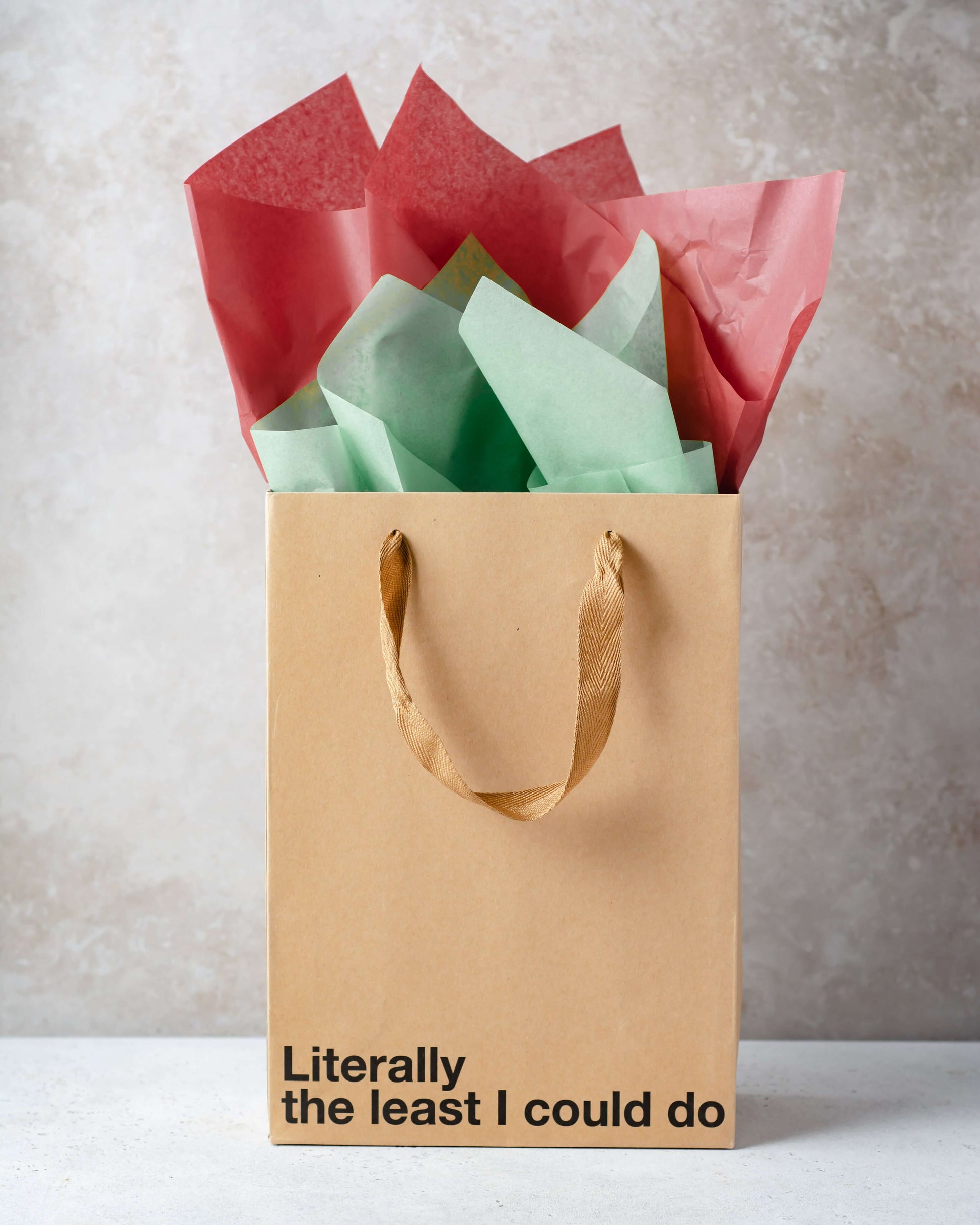 Funny gift bags featuring a kraft bag with the phrase 'Literally the least I could do' and colorful tissue paper.
