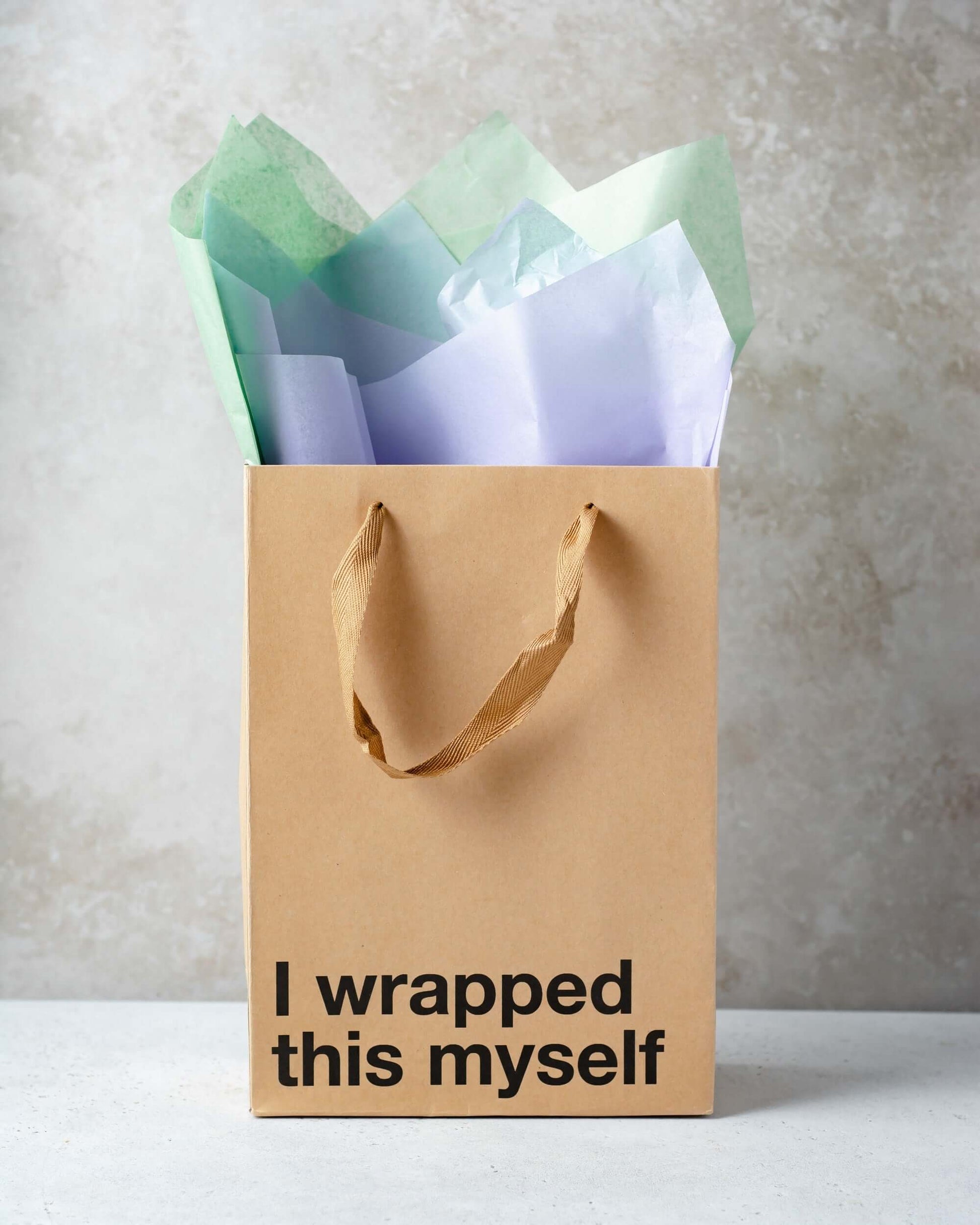Funny gift bag with kraft material and brown ribbon handle, wrapped with colorful tissue paper.