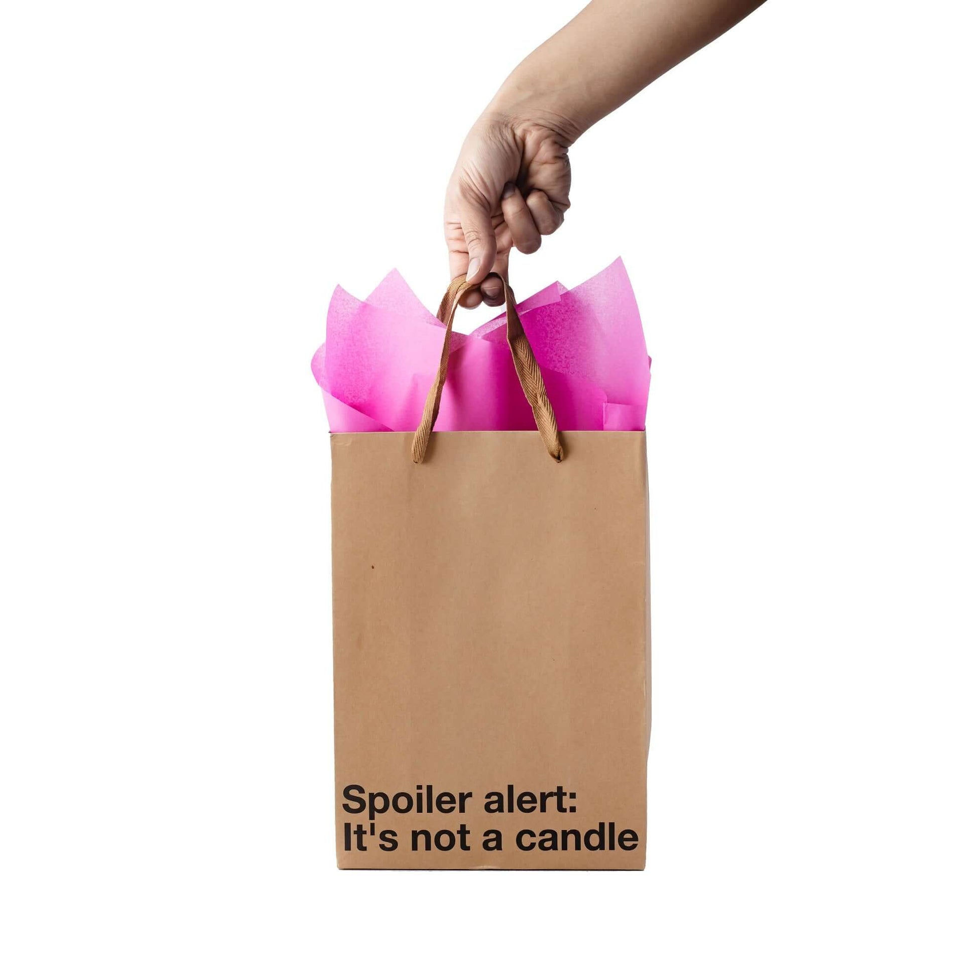 Funny gift bag that says 'Spoiler alert: It's not a candle' with pink tissue paper.