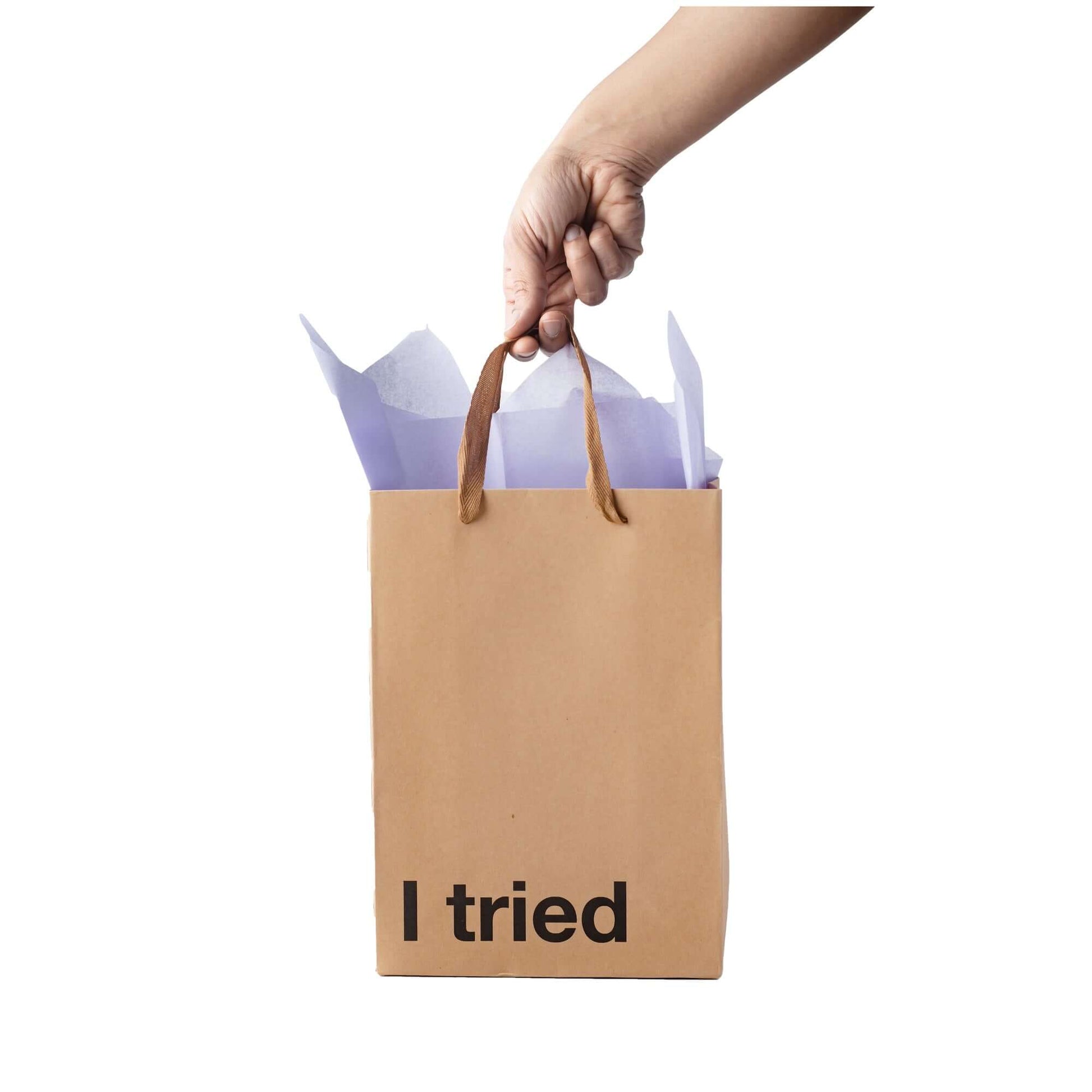 Funny gift bag with text 'I tried', held by a hand, featuring kraft material and ribbon handles.