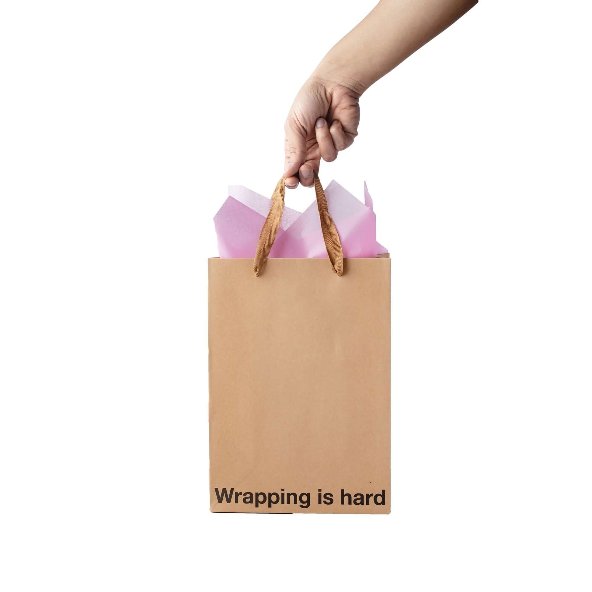 Funny gift bag with the text 'Wrapping is hard' held by a hand, featuring colorful tissue paper.
