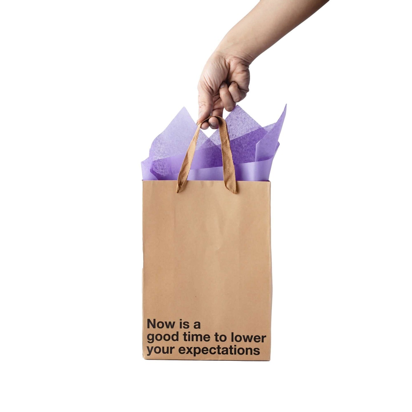 Funny gift bag reading 'Now is a good time to lower your expectations' with tissue paper on top.