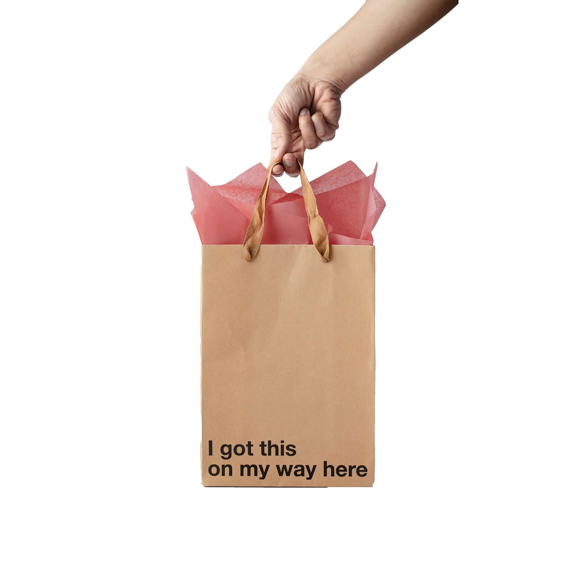 Funny gift bag saying 'I got this on my way here' with pink tissue paper. Kraft material with a brown ribbon handle.