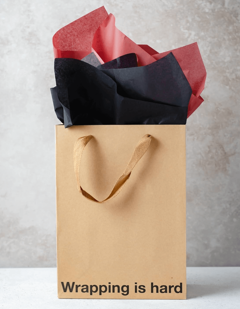 Brown kraft gift bag with colorful tissue paper saying 'Wrapping is hard' for funny gift bags.