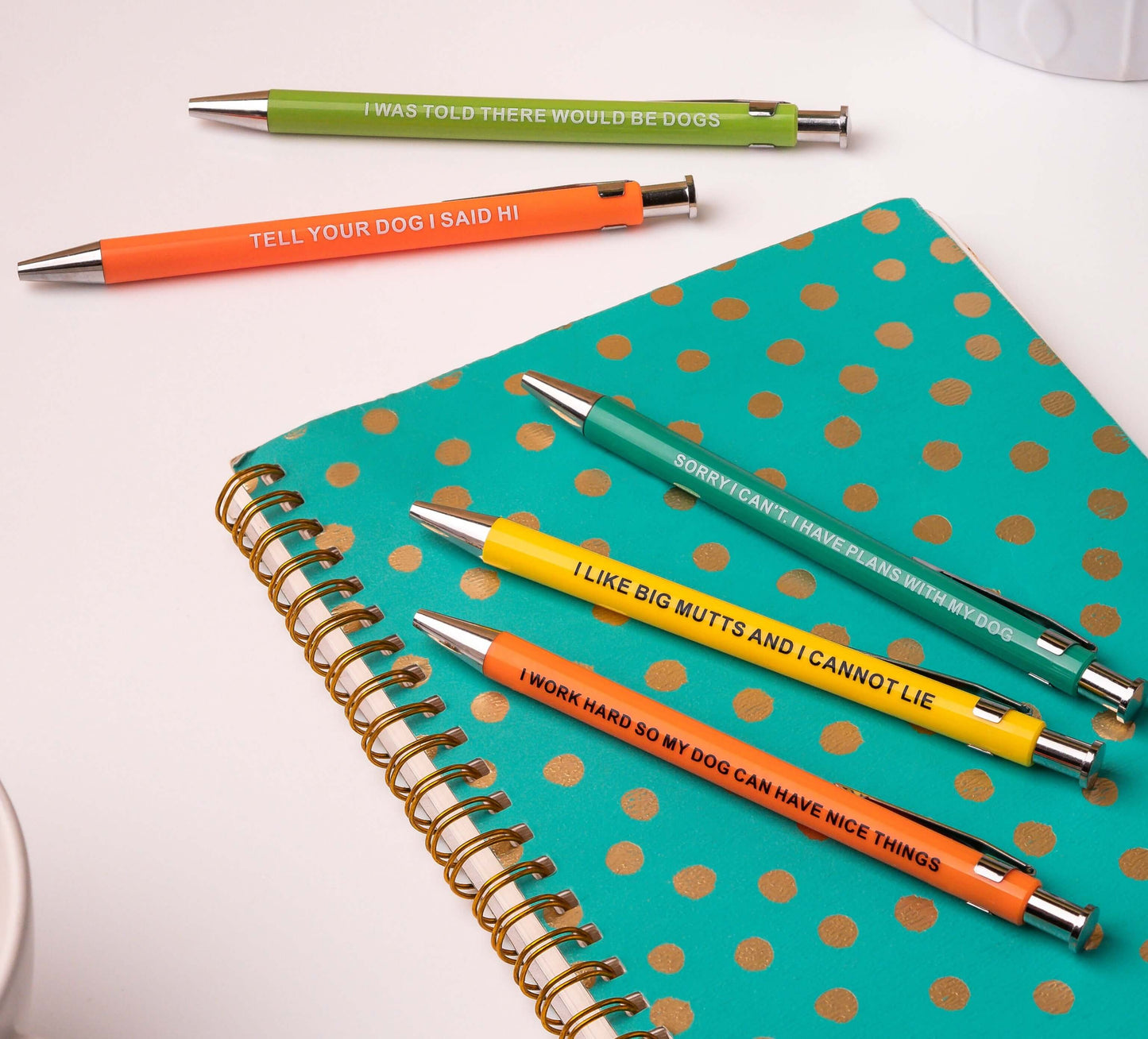 Colorful funny pens with dog-themed phrases on a notebook with gold polka dots.