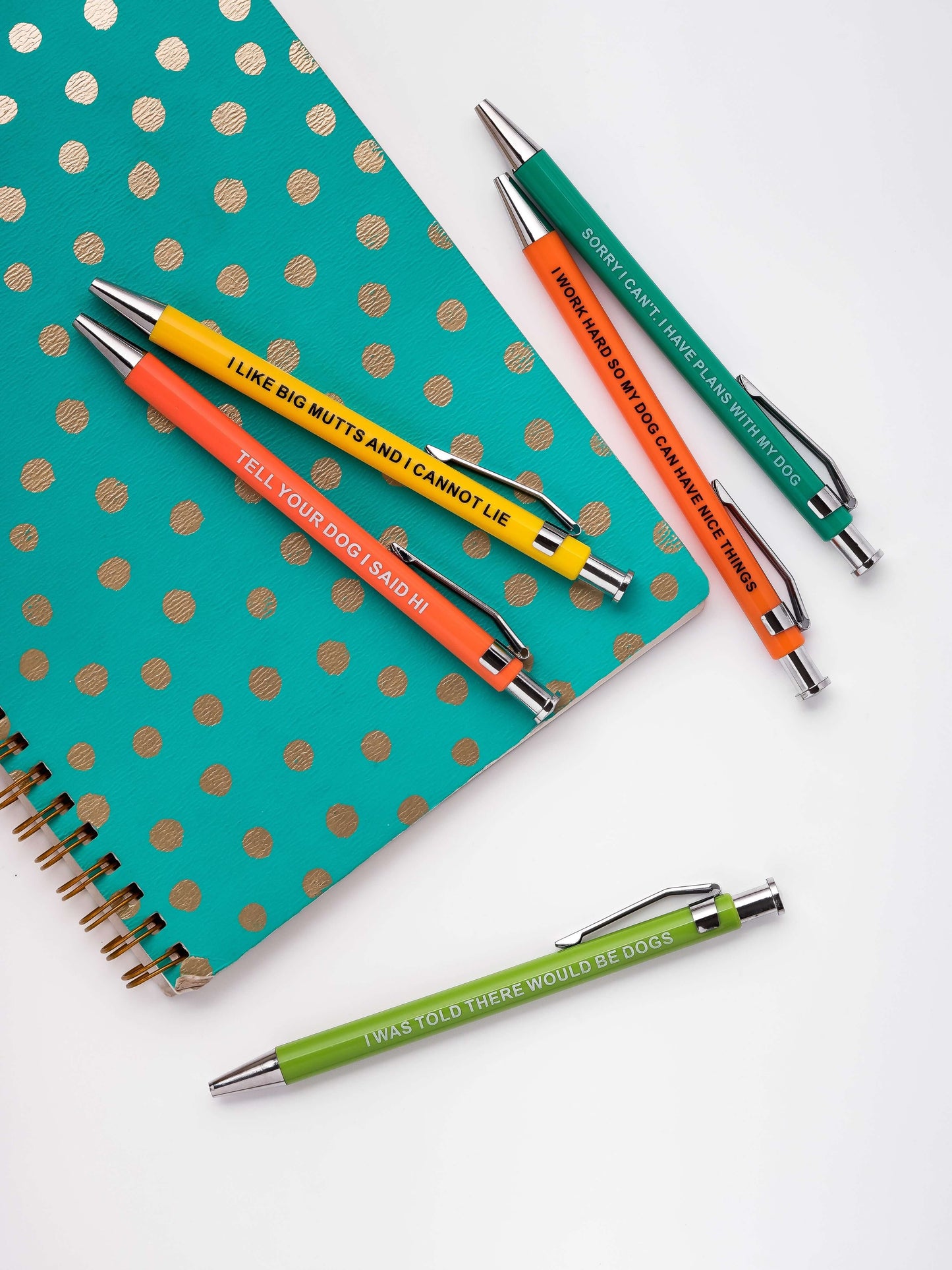 Colorful funny pens with humorous dog phrases on a teal notebook with gold polka dots.